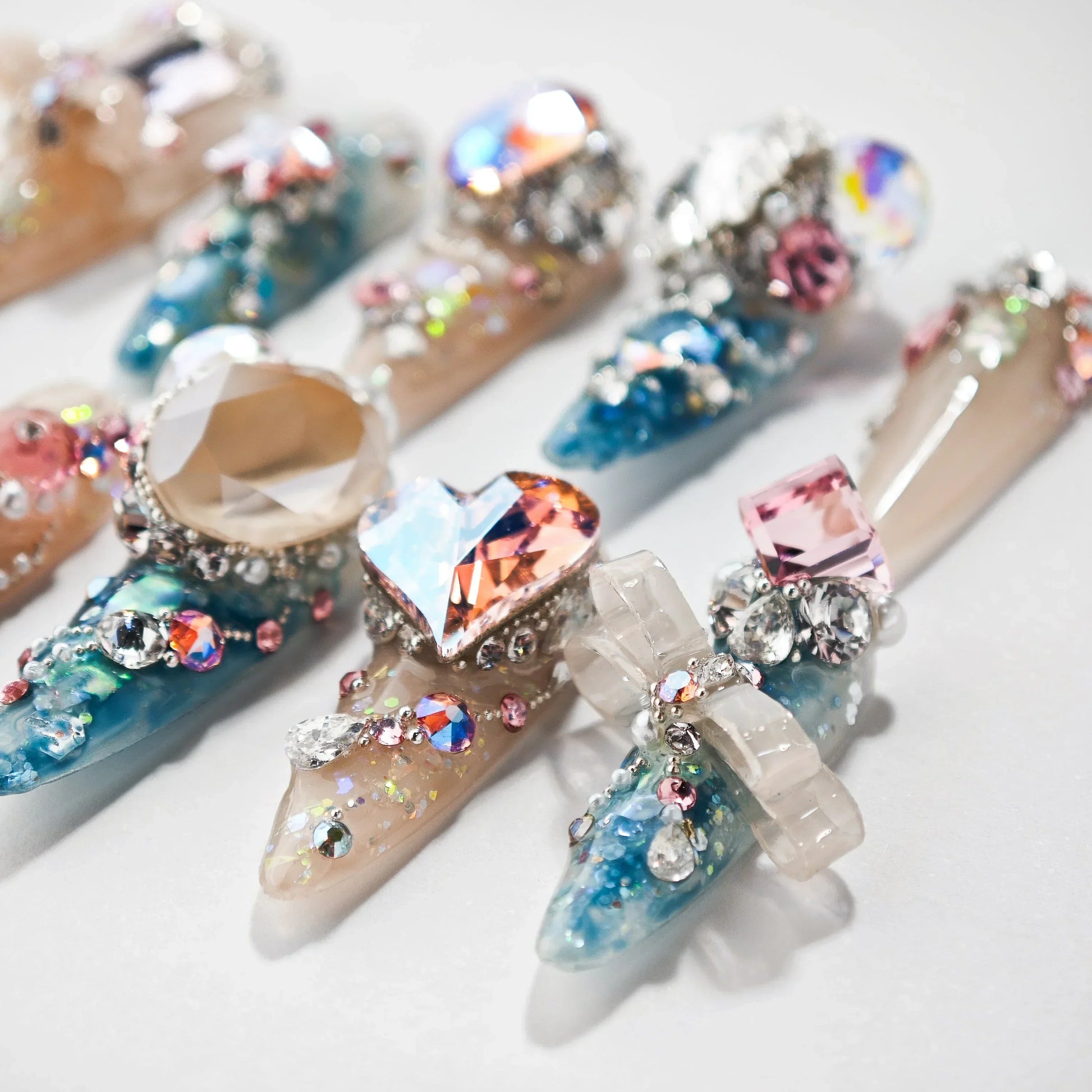 Handmade press-on nails with blue, beige, and pink base, decorated with large gemstones and crystals