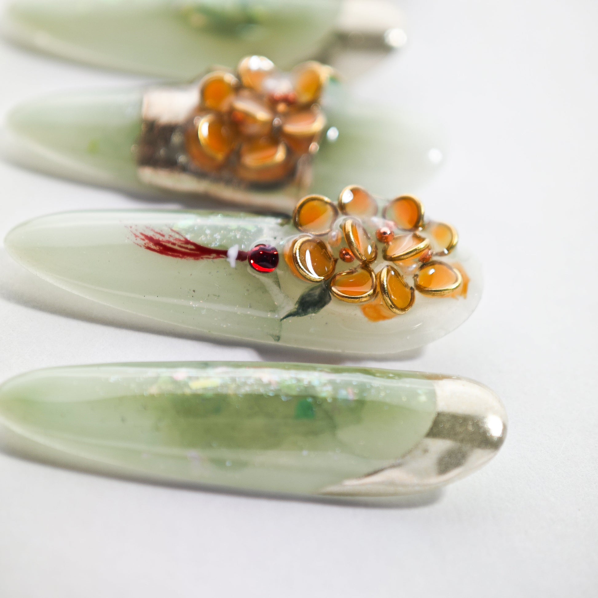Handmade press-on nails with light green base, gold tips, and 3D orange floral accents