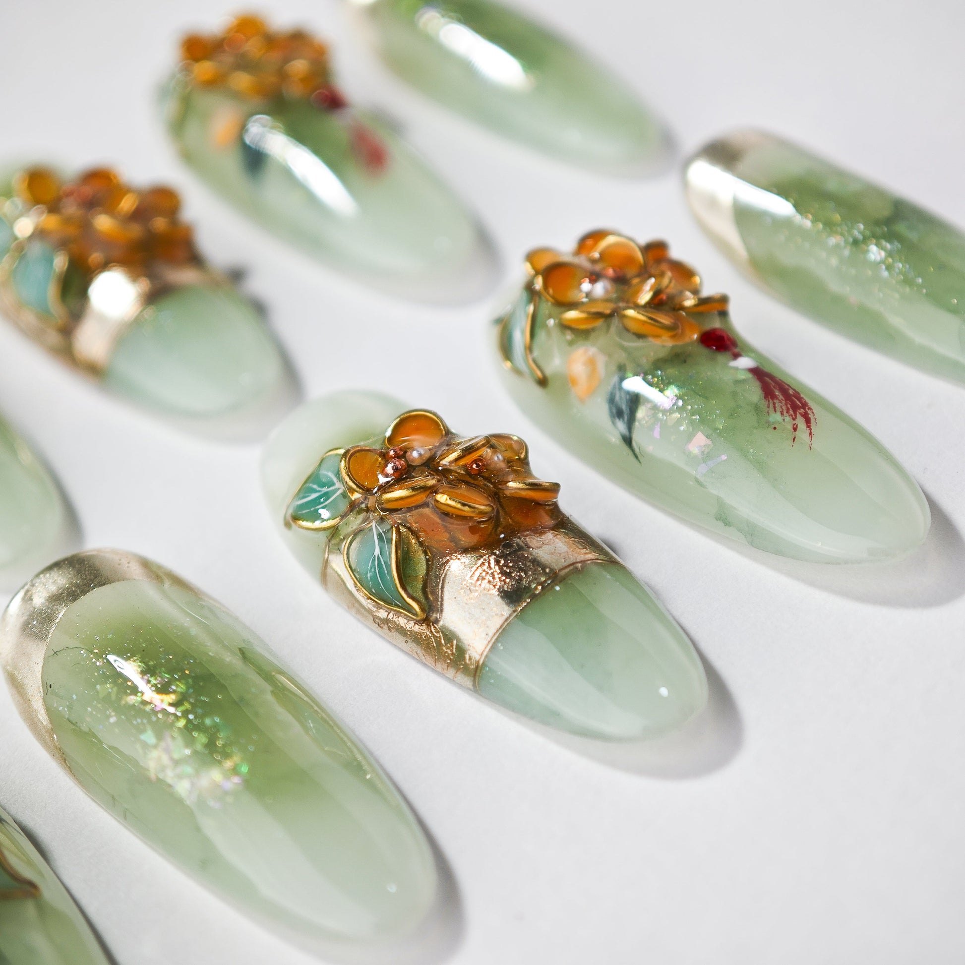 Green handmade press-on nails with 3D orange floral art and gold foil accents on white background