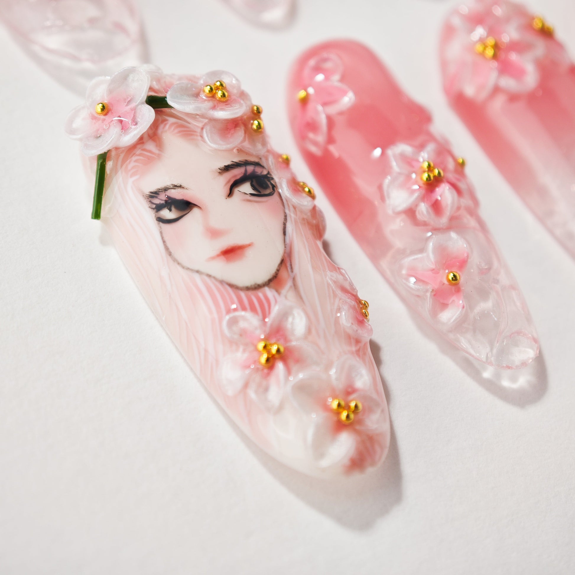 Handmade press-on nails with 3D floral art and anime-inspired face design in pink tones