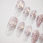 Handmade pink press-on nails with crystal accents and 3D floral design on a white background