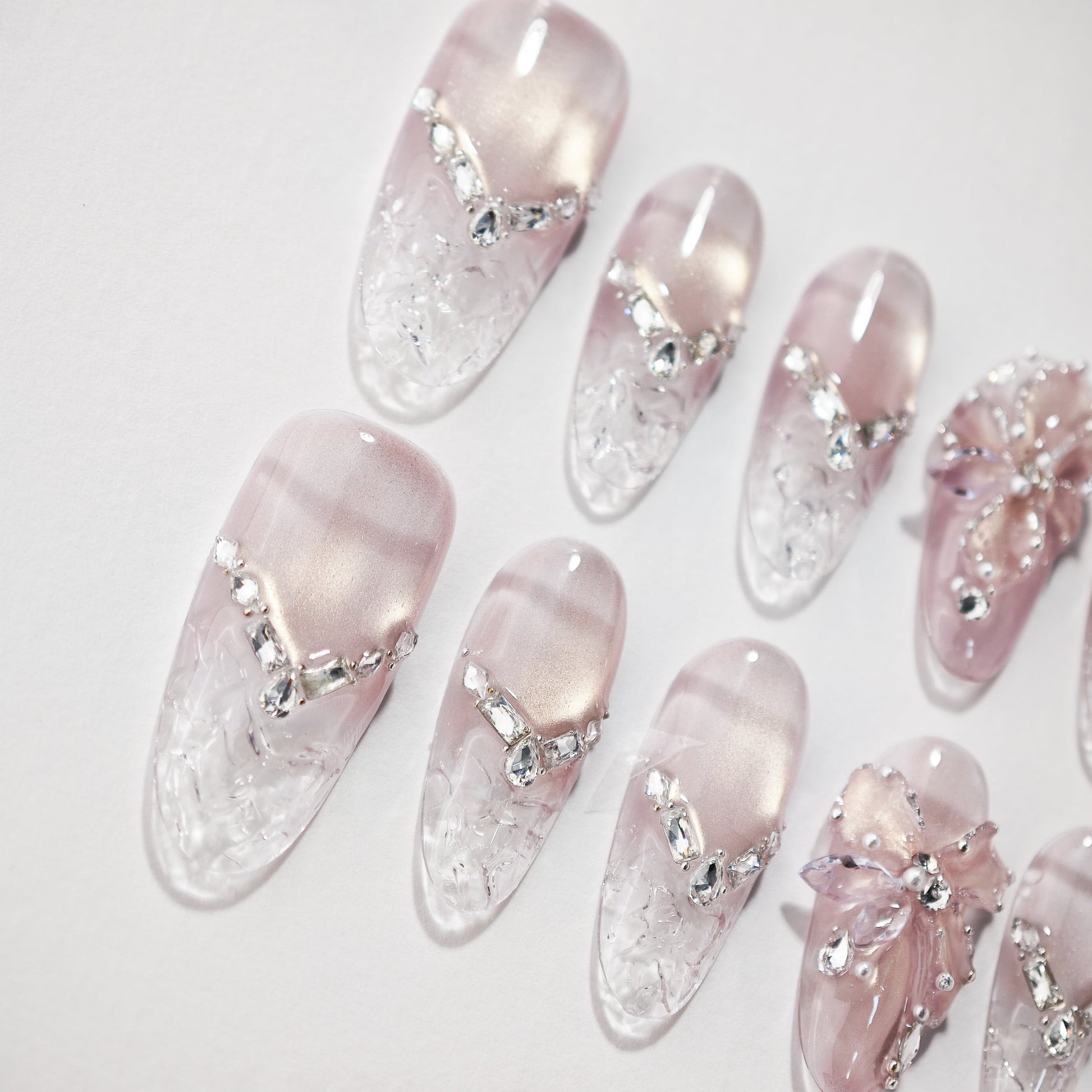 Handmade pink press-on nails with crystal accents and 3D floral design on a white background