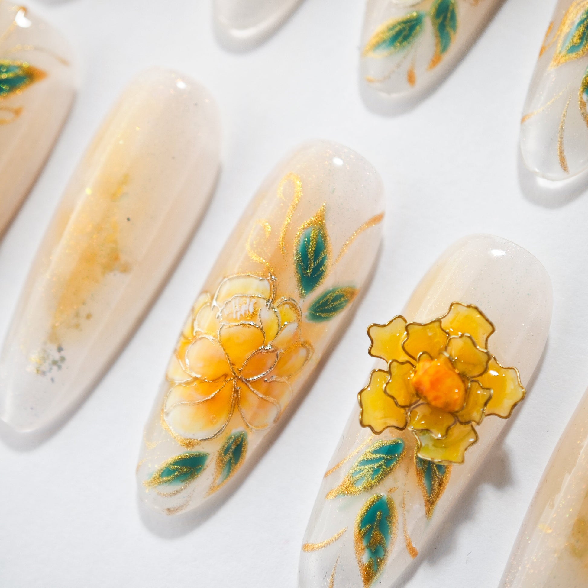 Handmade press-on nails with yellow floral designs and green leaf accents on a nude base