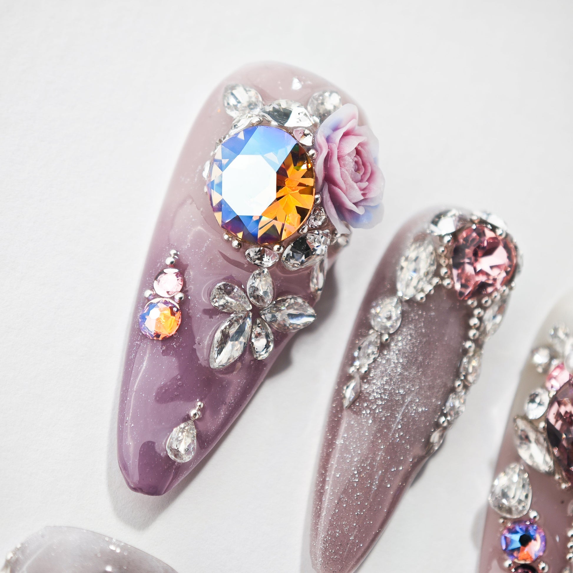 Handmade press-on nails with purple base, rhinestones, floral 3D design, and crystal gems
