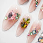 Long nude press-on nails with colorful gem and crystal embellishments, ombre design, glitter accents.