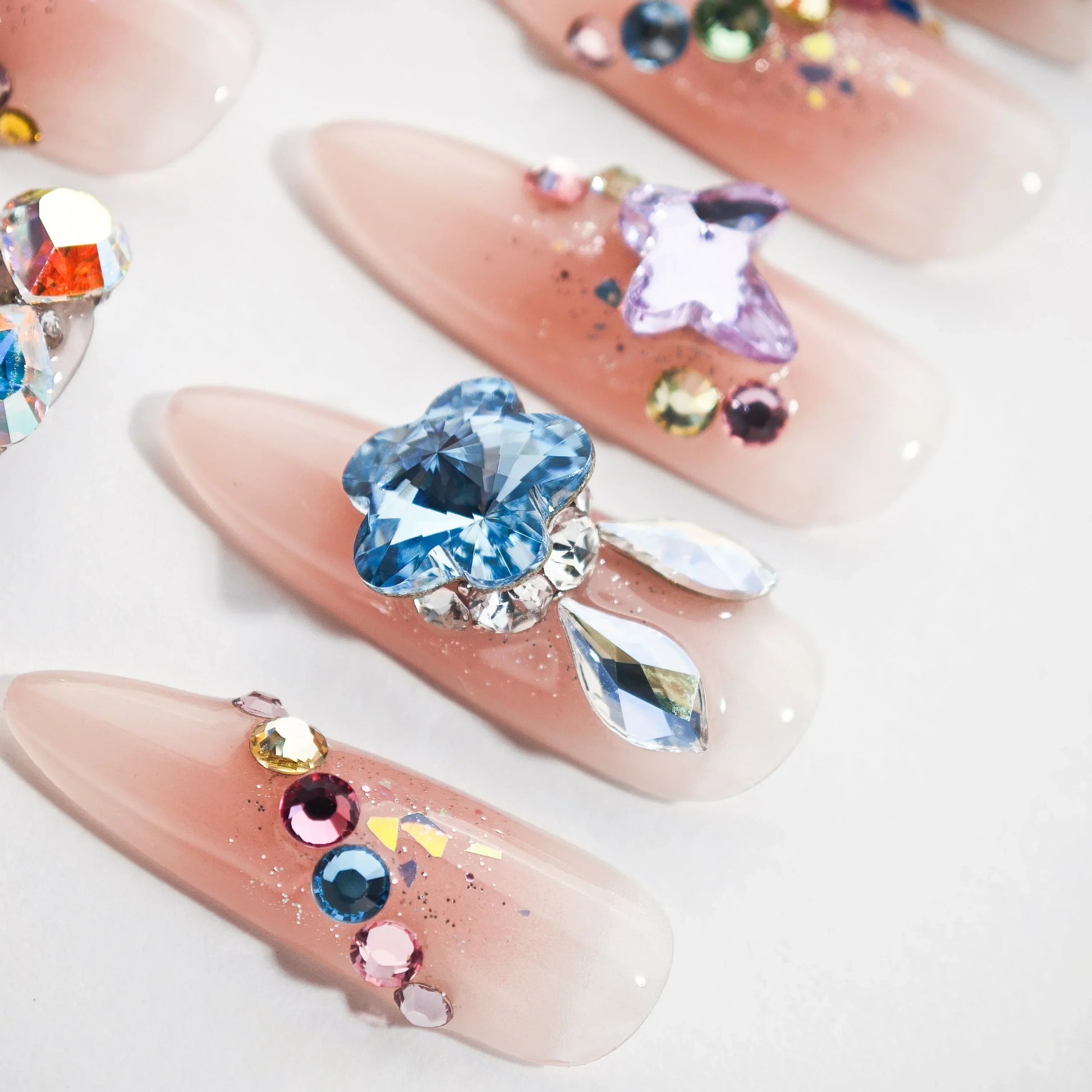Handmade press-on nails with nude pink base, adorned with colorful crystals and rhinestones