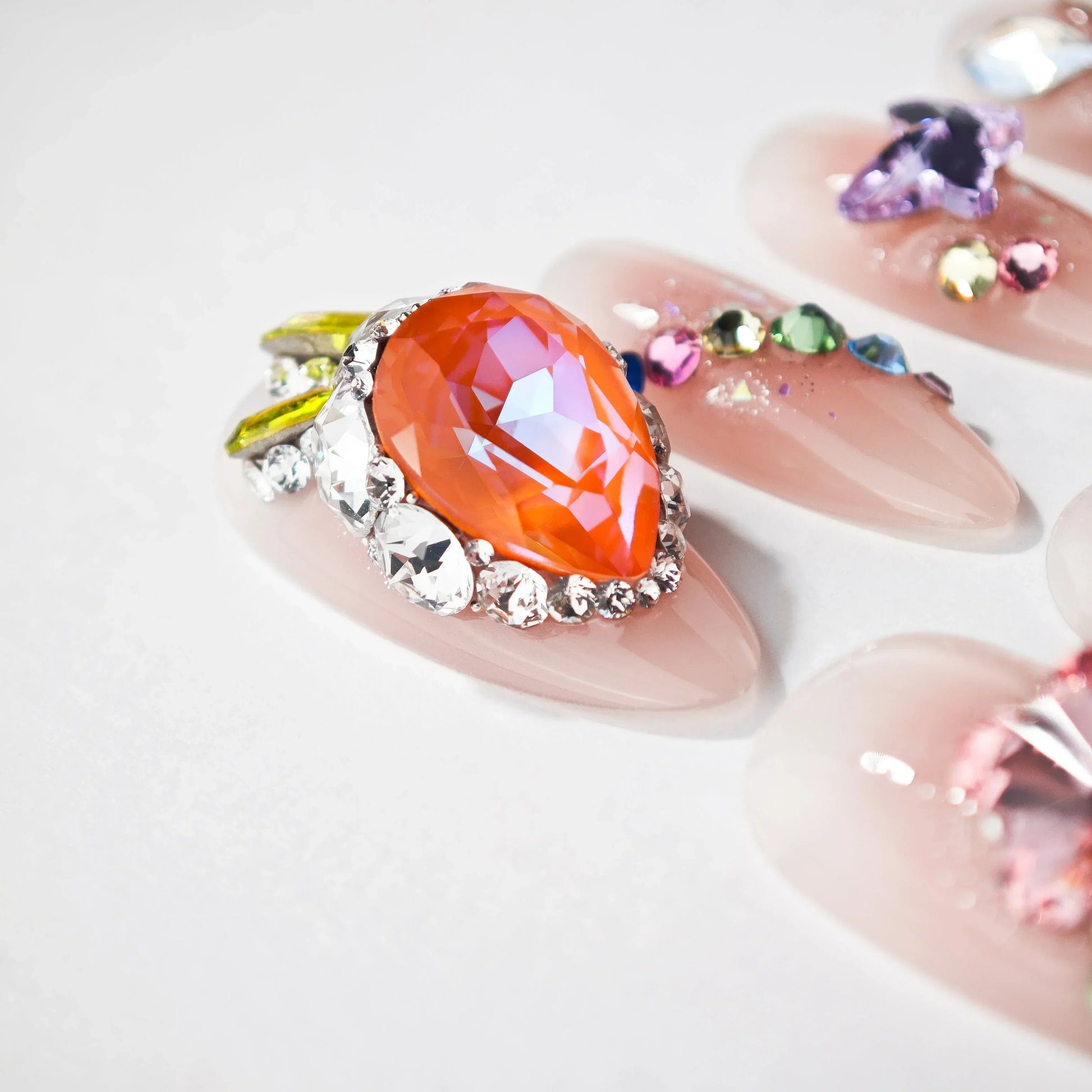 Handmade press-on nails with nude base, large orange gemstone, and colorful rhinestone accents