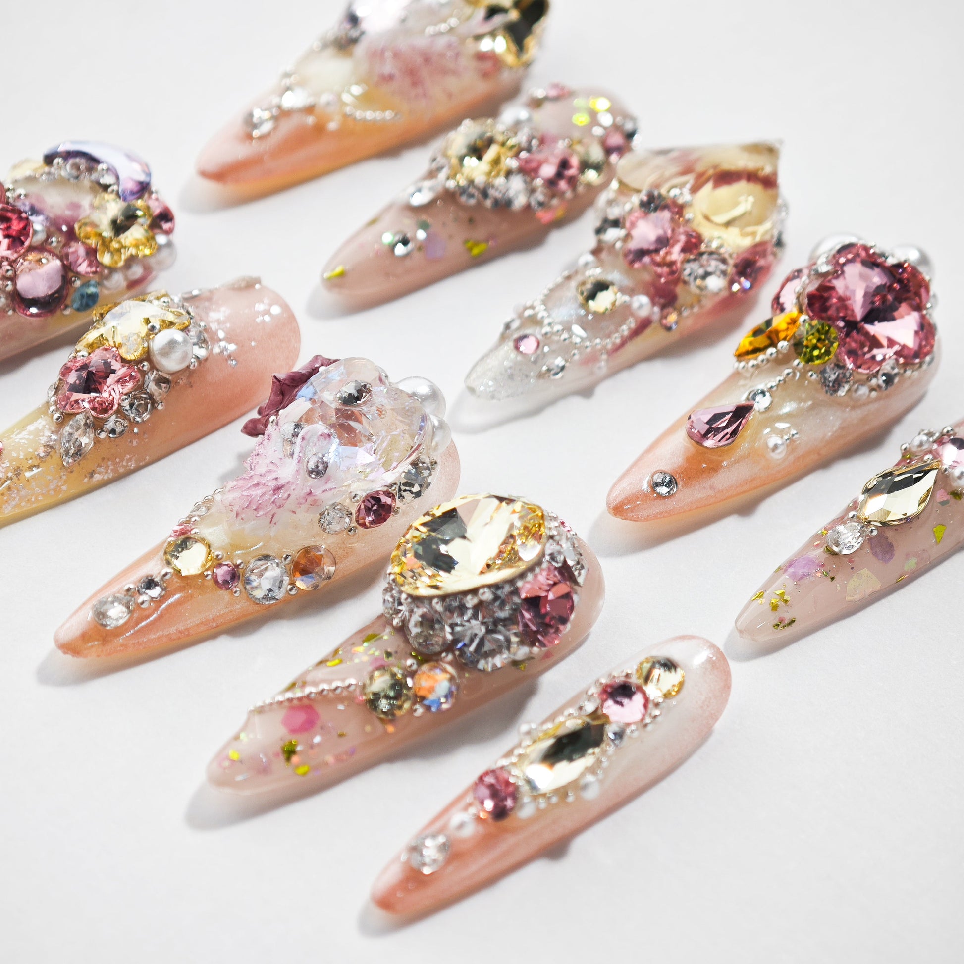 Handmade press-on nails with pink, gold, and crystal gem embellishments on a white background