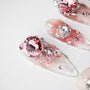 Handmade press-on nails with pink rhinestones, glitter, and silver gems on a white background