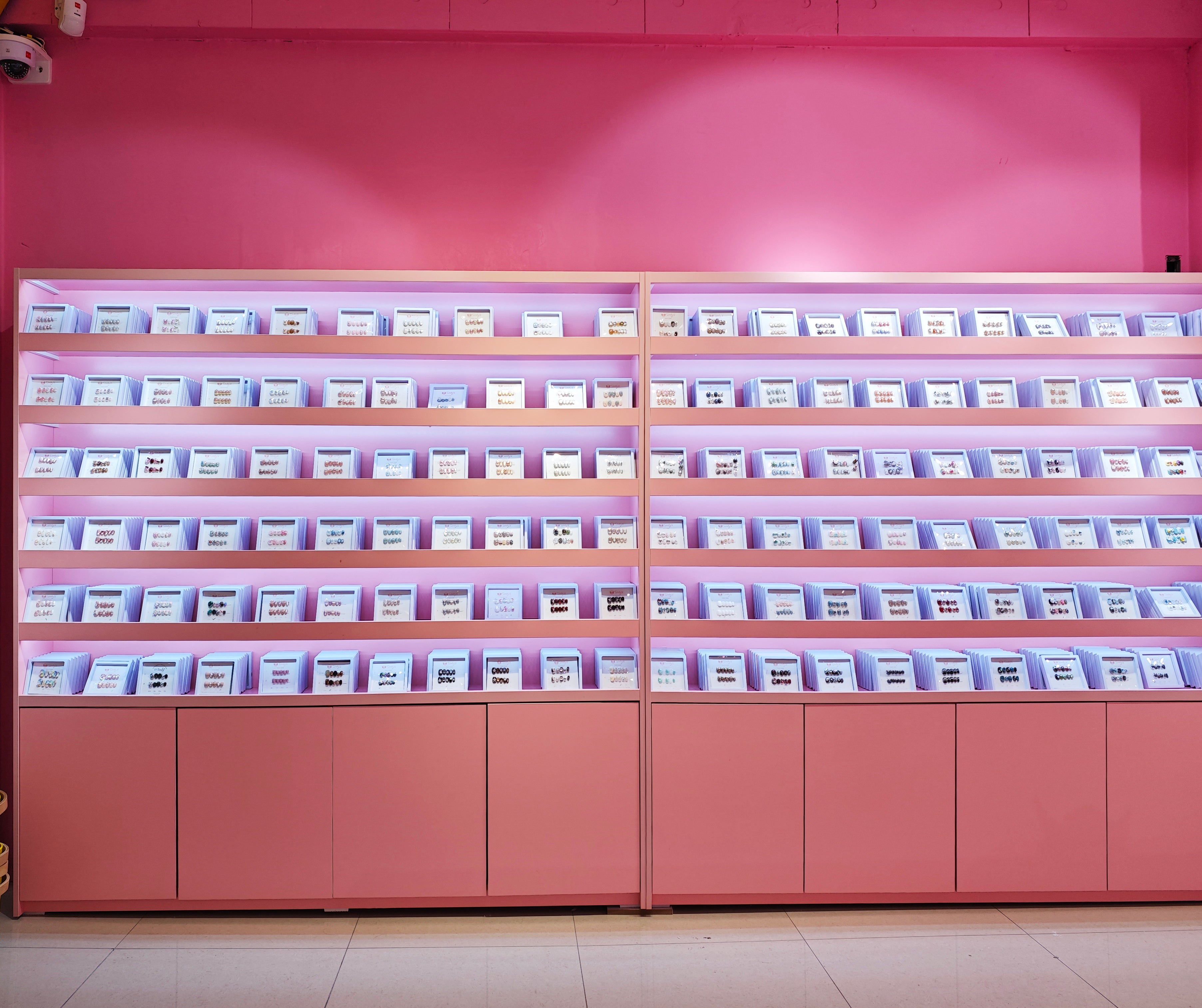 Display of handmade press-on nail sets in pink shelving against a pink wall